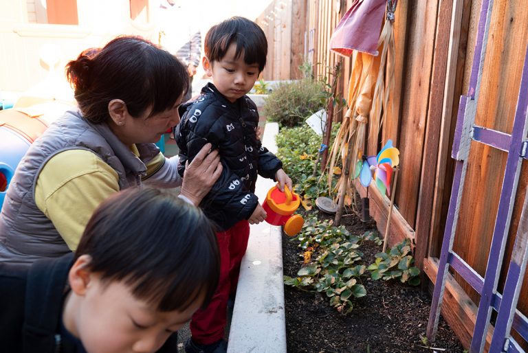 A child watering plants with a teacher in family child care